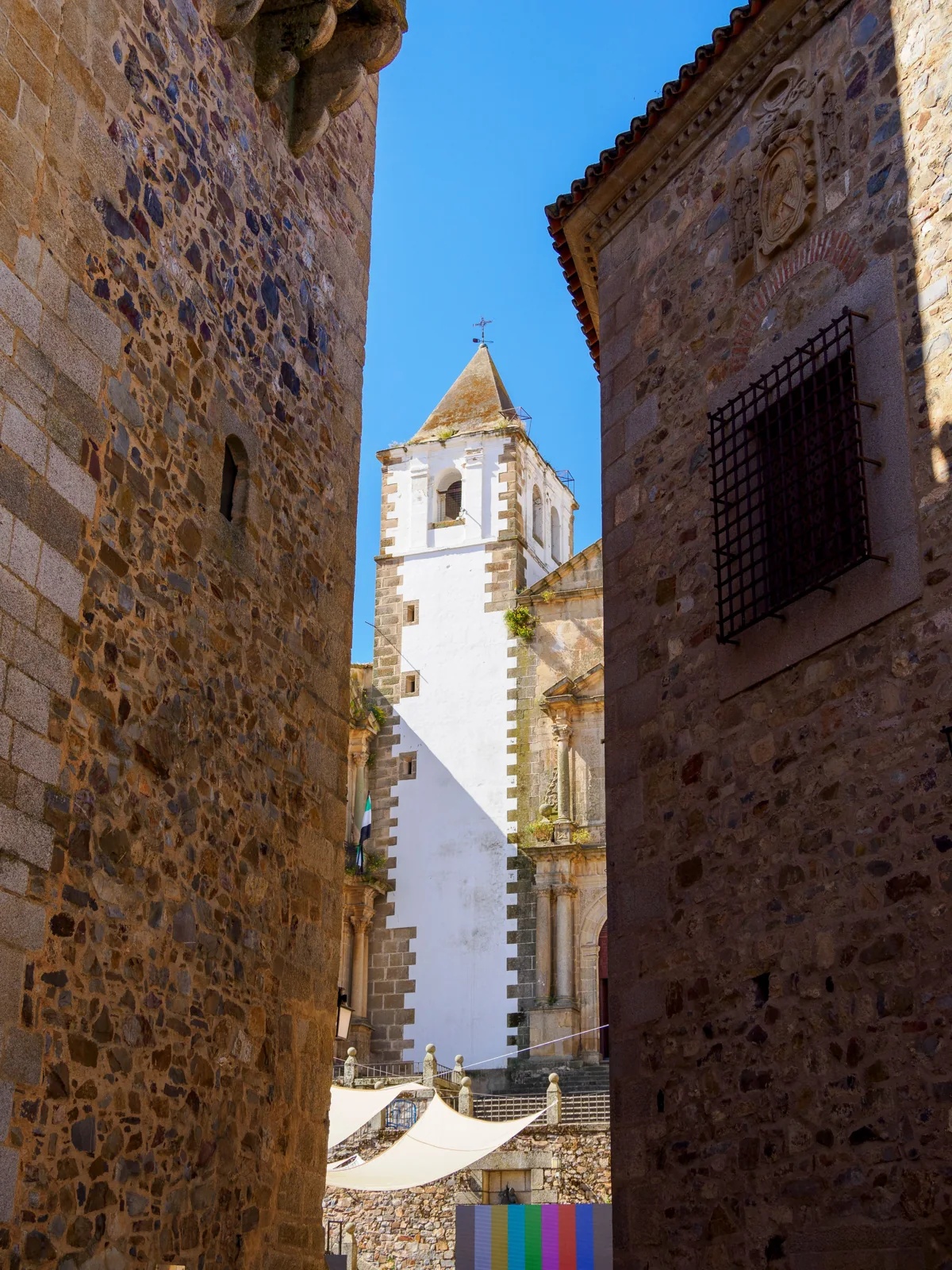 Weißer Turm der Kirche San Francisco Javier in Cáceres zwischen zwei historischen Steinmauern