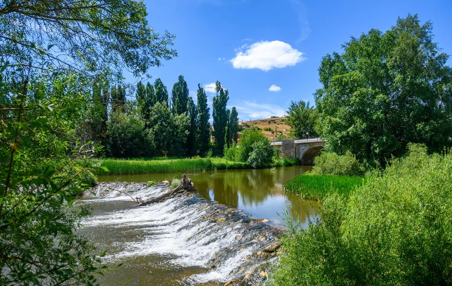 Duero bei Soria mit grünen Ufern, kleinem Wehr und einer Steinbrücke