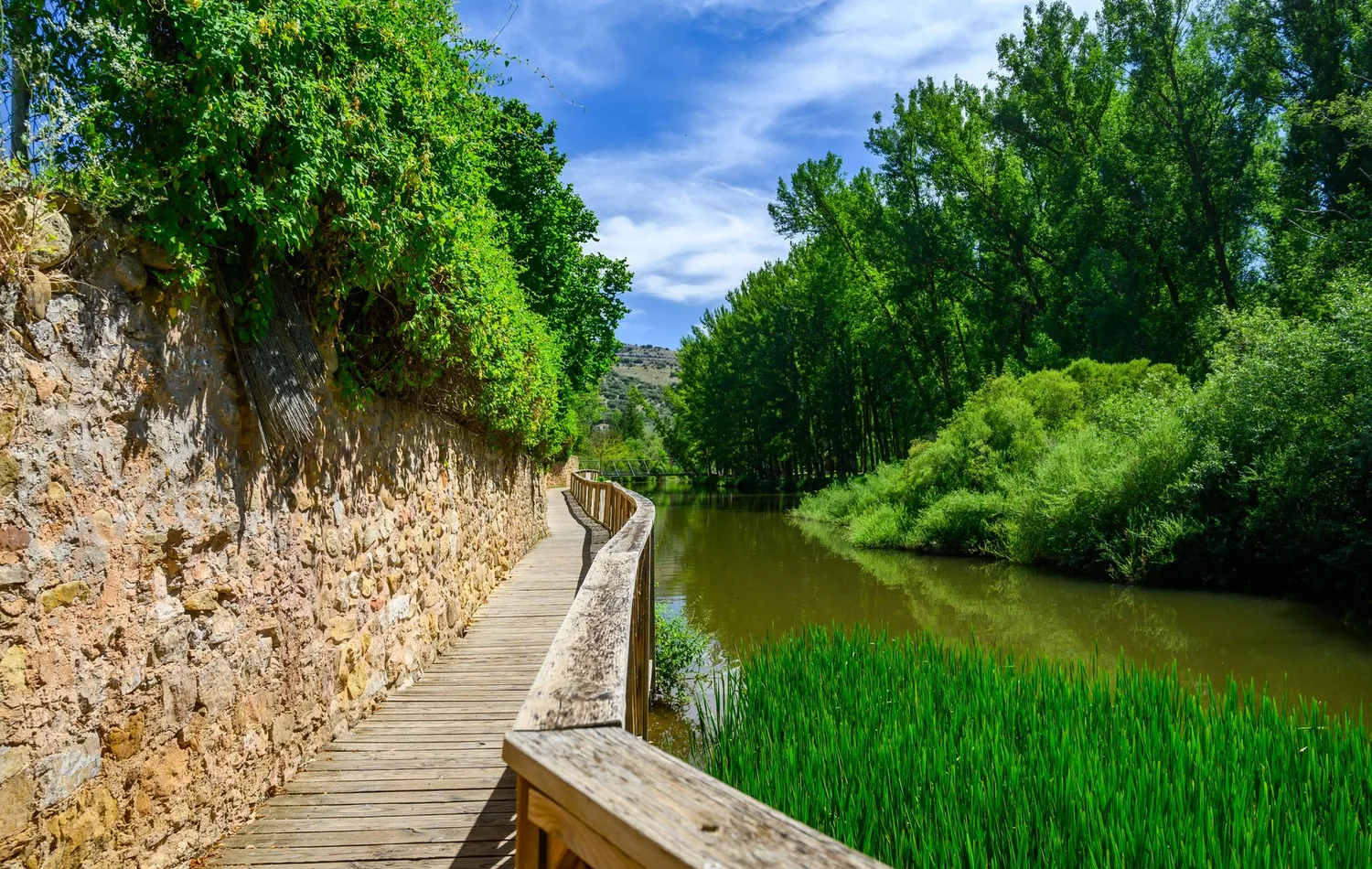 Hölzerner Uferweg am Duero in Soria zwischen Steinmauer und grüner Flusslandschaft